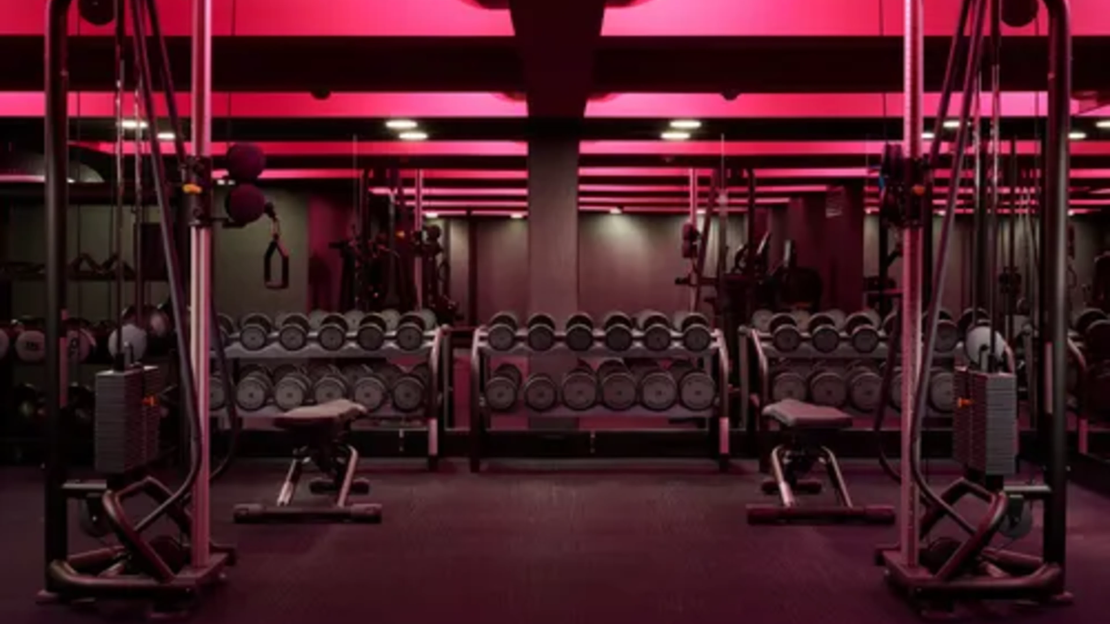 Advanced strength floor with dumbbells and cable machines under red lighting
